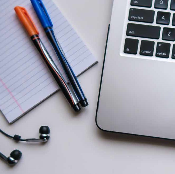 A laptop computer, pens, a notepad and headphones sit on a desk