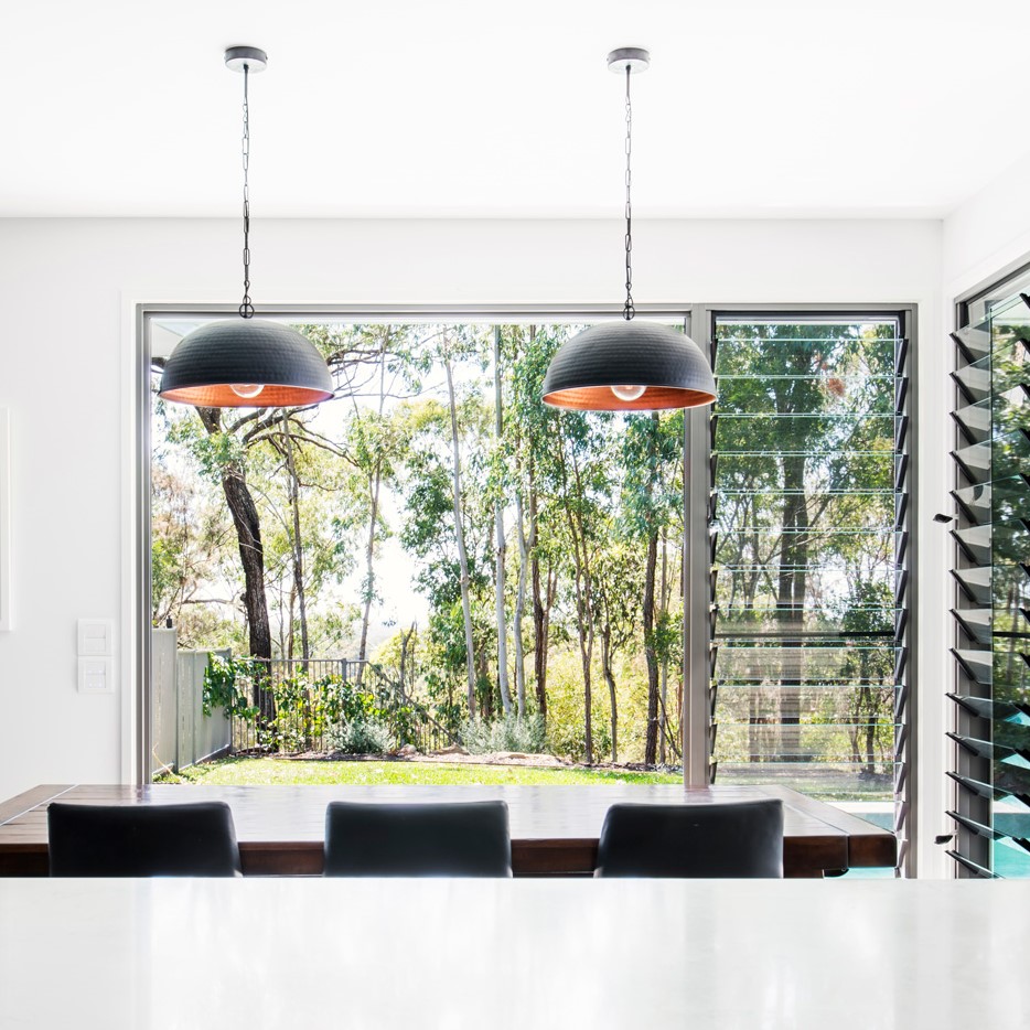 A view outside a large home window with green grass and bushland